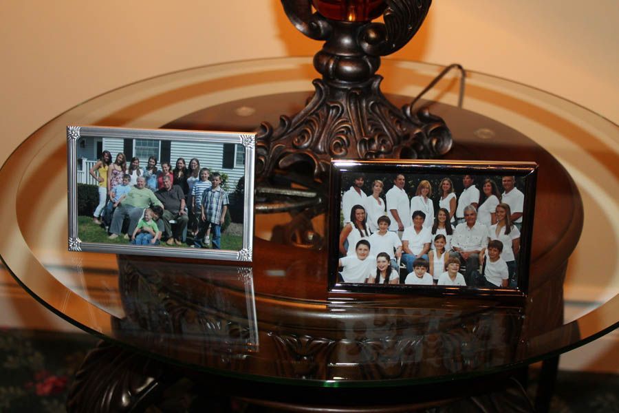 Two framed family photos on a glass-topped table, beside a lamp with a decorative base.