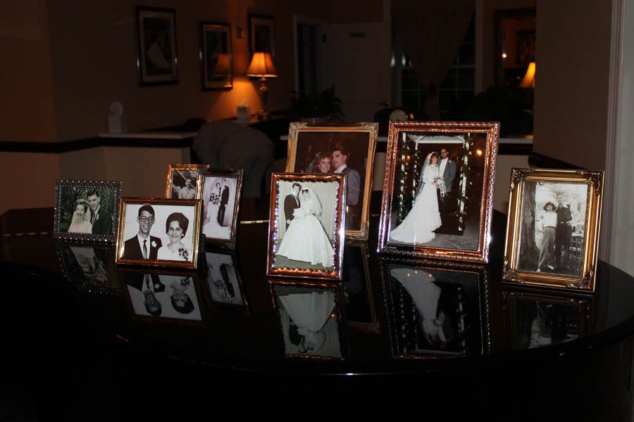 Wedding photos in ornate frames displayed on a shiny black surface, illuminated by warm light.