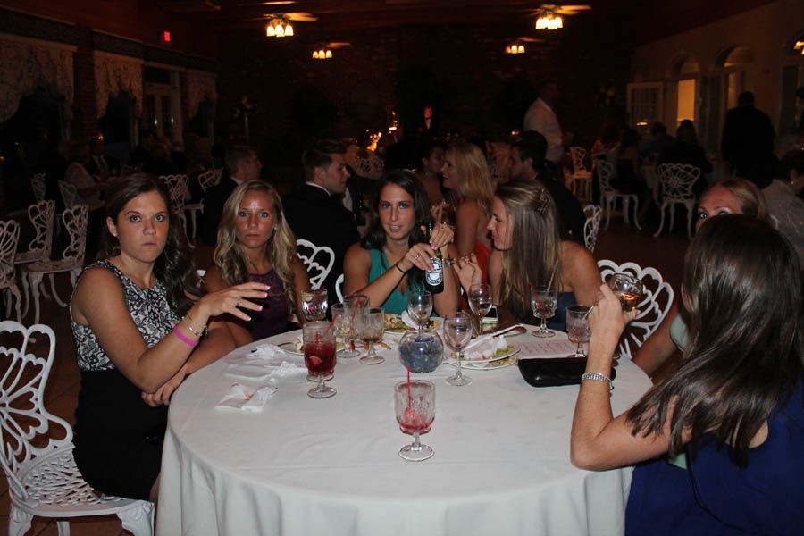 Guests at a party seated around a white tablecloth. Several women are at a round table, engaged in conversation.