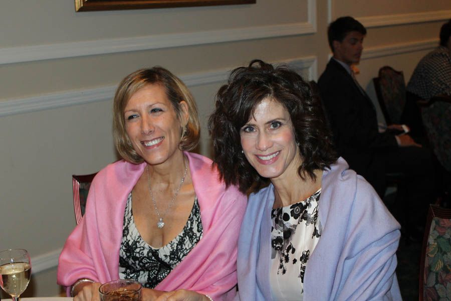 Two smiling women pose indoors, wearing shawls over patterned dresses.