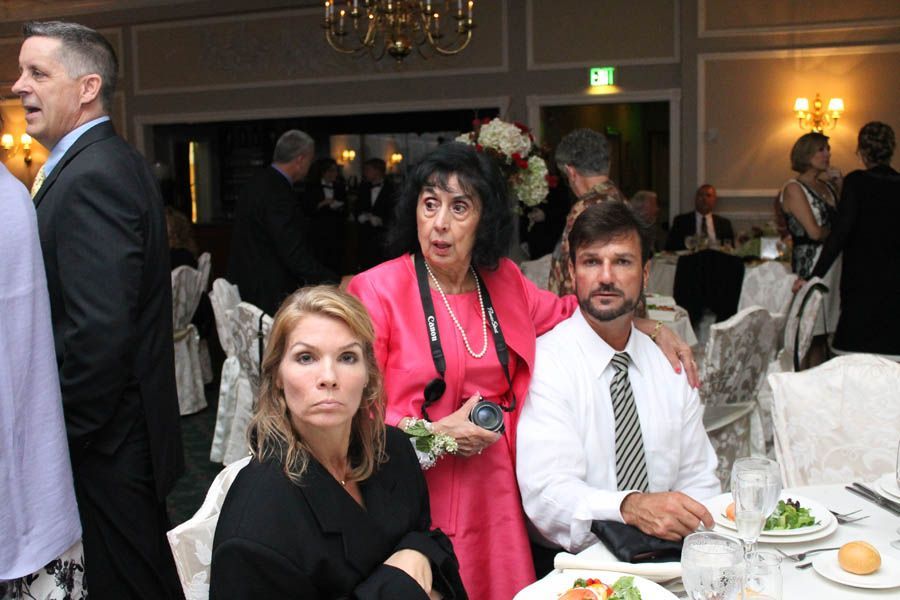 People at a formal event; woman in pink talking, others at tables.