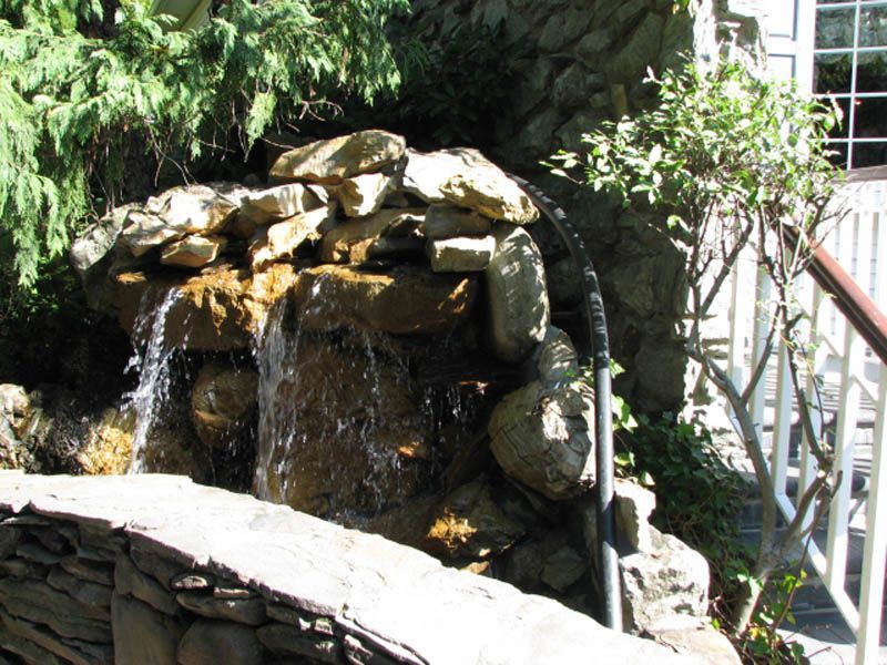 Waterfall cascading over rocks in a garden setting, adjacent to a building.