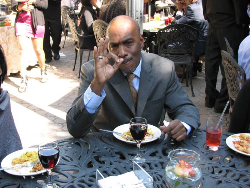 Man in suit at outdoor table, gesturing 
