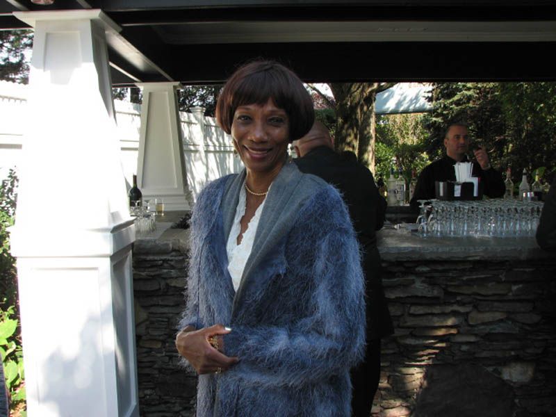 Woman wearing a blue fuzzy sweater stands outside near a stone bar.
