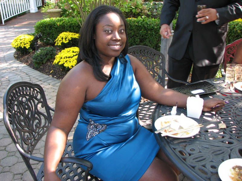 Woman in blue dress sitting at outdoor table, smiling.