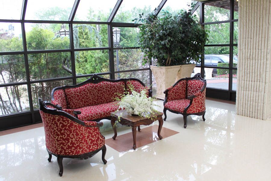 Elegant seating area with red patterned furniture, small table, and potted plant, beside large windows.