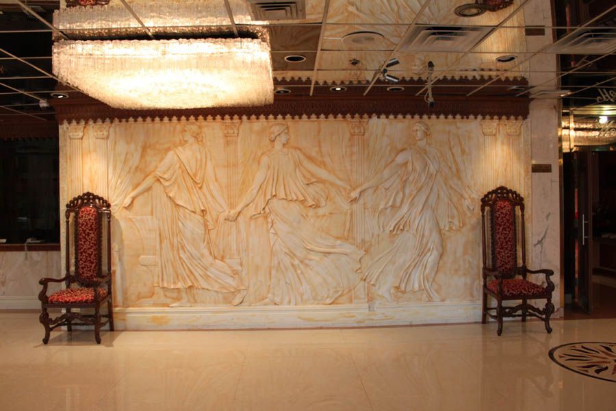 Wall relief of dancing figures, flanked by ornate chairs. Large chandelier above.