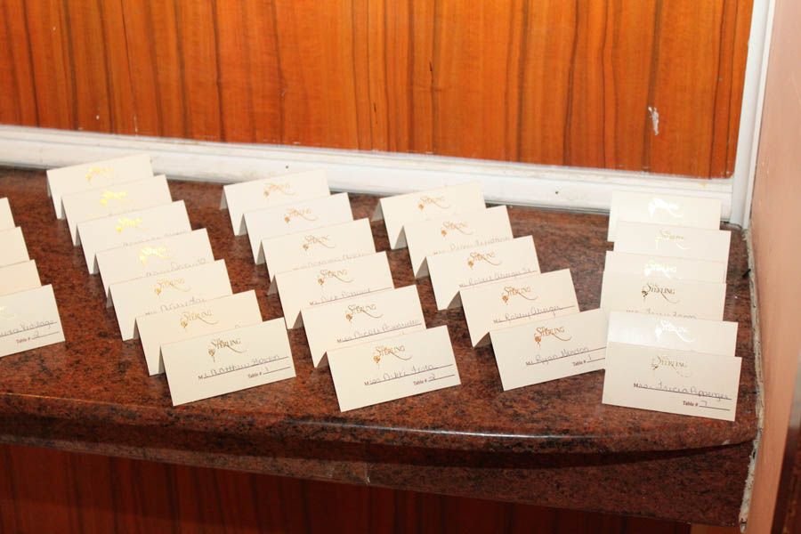 Cream-colored place cards arranged on a marble surface in front of a wood-paneled wall; some have gold accents.