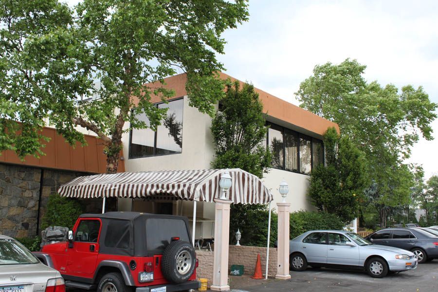 Building with awning, trees, and parked cars in front. A red Jeep is in the foreground.