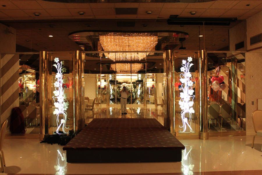 Stage in a golden-trimmed room with mirrored walls, a chandelier, and a brown platform.