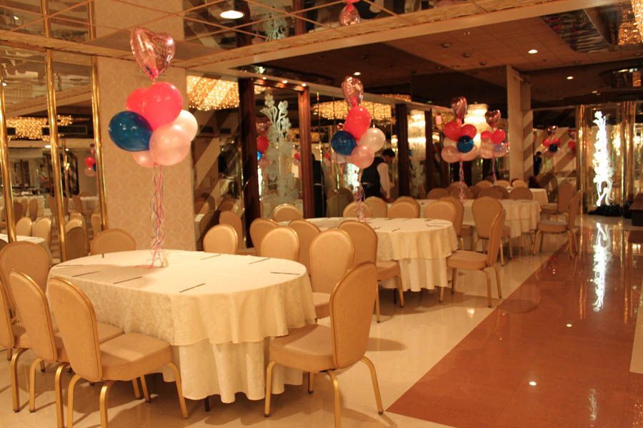 Banquet hall with round tables set with white tablecloths, gold chairs, and balloon centerpieces.
