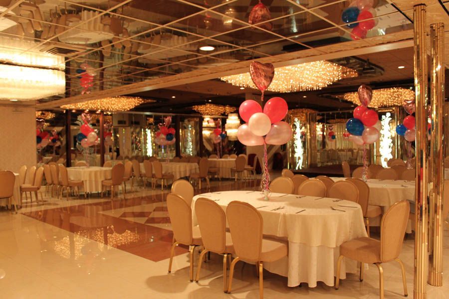 Banquet hall with round tables set for a celebration, gold chairs, mirrored ceiling, and balloon decorations.