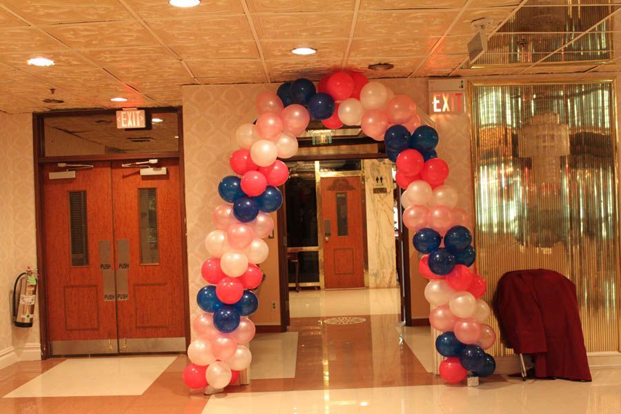 Balloon archway in pink, white, and blue over an entryway with wooden doors and a fire extinguisher.