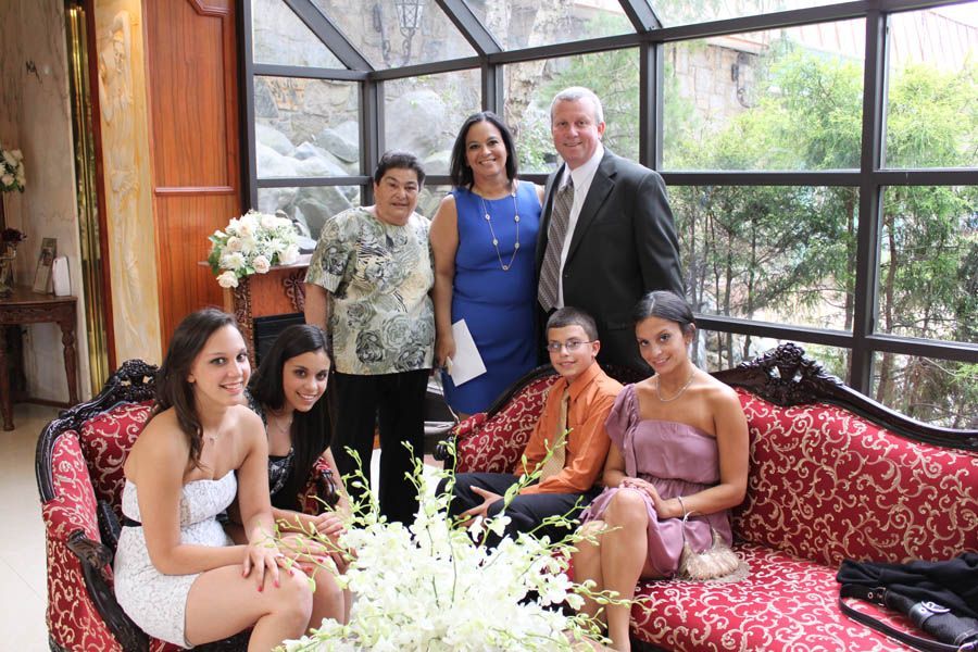 Family posing for photo in sunroom. Includes a red couch and white floral arrangement.