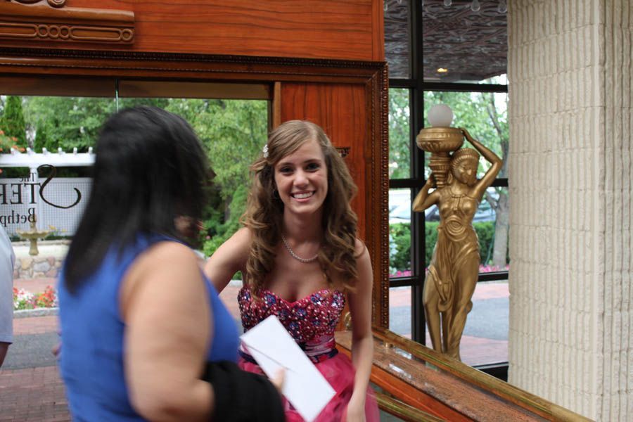 Woman in prom dress smiles by a golden statue at an event entrance.