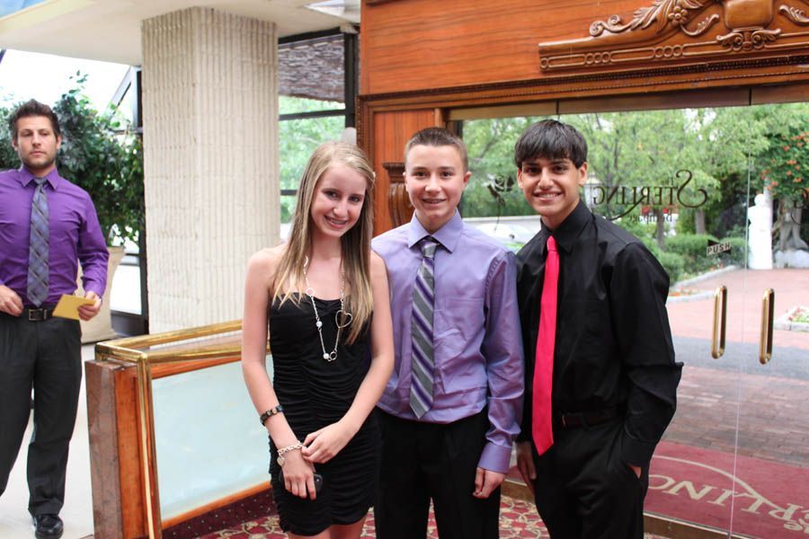 Four people in formal attire pose near a doorway. Two men wear black and purple shirts. A woman wears a black dress.