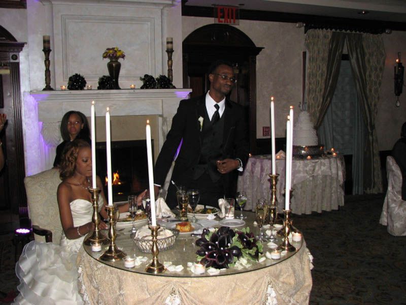 Bride and groom at reception table. Candles surround the table with a man speaking.
