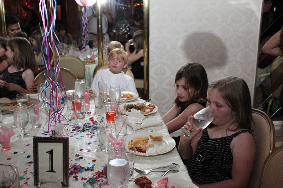 Children at a decorated table, some eating and drinking at a party.