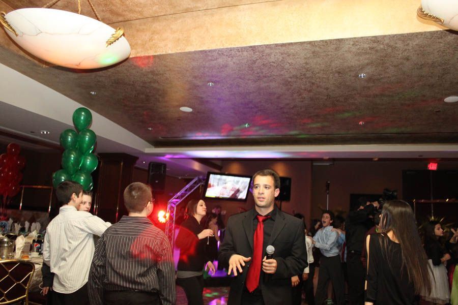 People dancing at a party; DJ with microphone, balloons, and disco lighting in a decorated room.