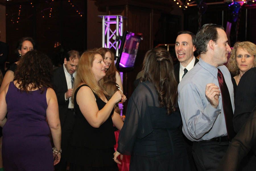 People dancing at a party, in a dark room.  Purple, black, and red attire.  A DJ light display is visible.