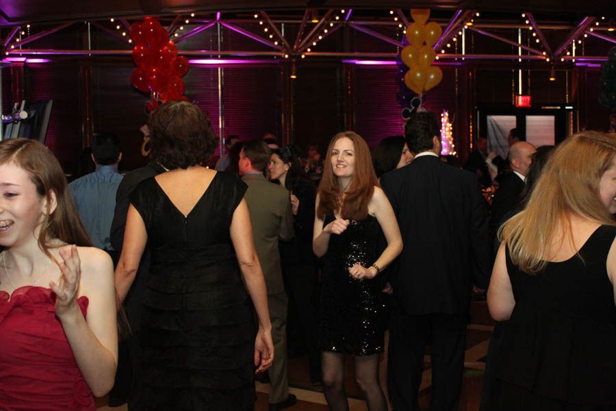 People dancing in a room lit with purple lights and balloons. One woman in a black dress is the focus.