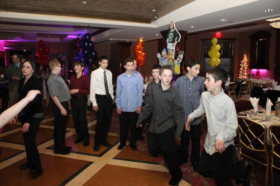 Boys in button-down shirts and dress pants at a party, with balloons and tables in the background.