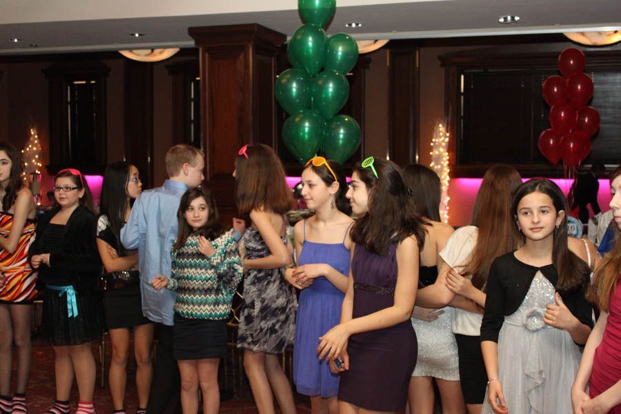 Group of young people at a party, standing and talking. Green and red balloons in background.
