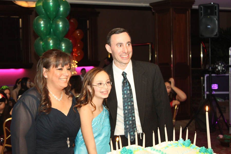 Family smiling by a birthday cake at a party with balloons.