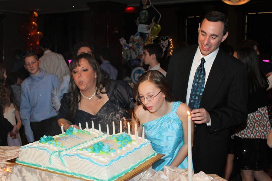 People blowing out candles on a cake at a party, man in suit holds a lit candle.