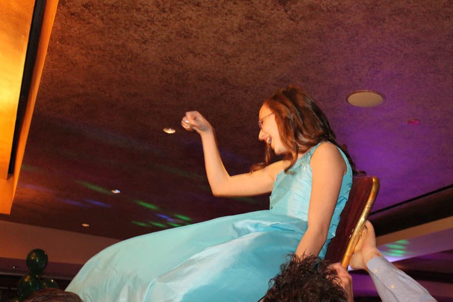 Woman in blue dress being lifted on a chair, smiling, indoors with disco lights.