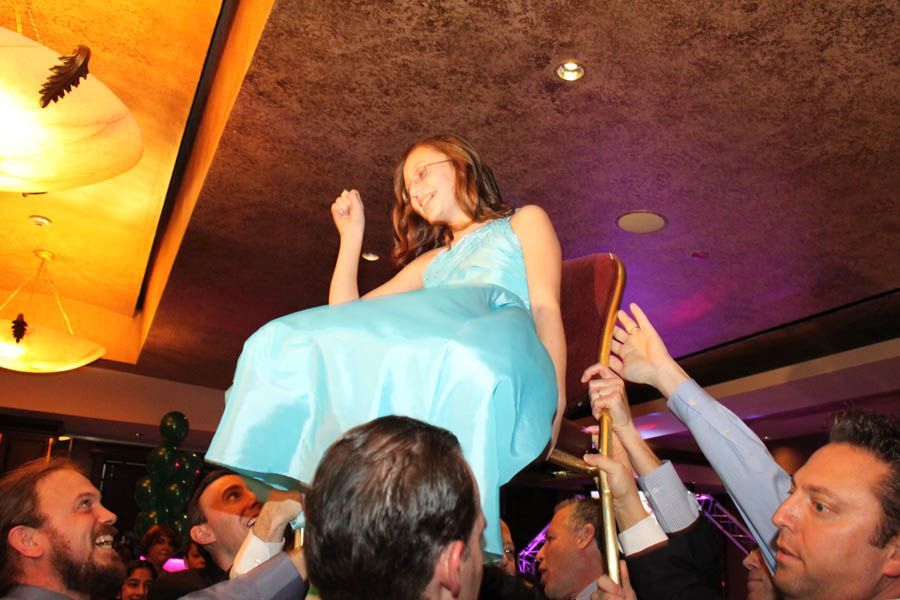 Woman in blue dress being lifted on a chair by a group of people, celebratory indoor setting.