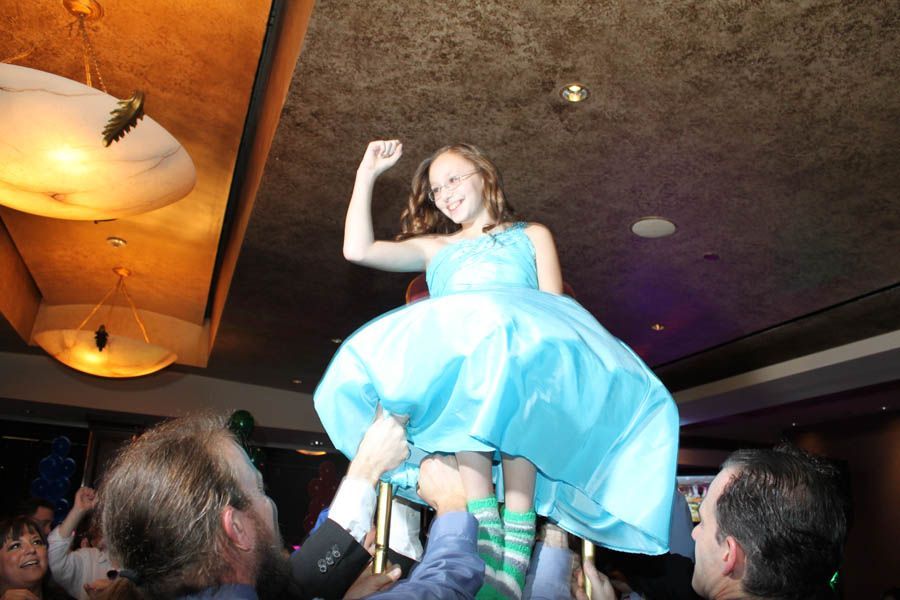 Girl in blue dress raised up in the air by people, celebrating, indoor event.