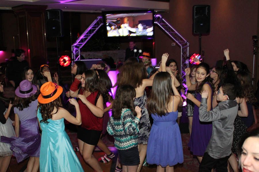 Teenagers dancing at a party with lights and a DJ. Many wearing dresses, some with hats.