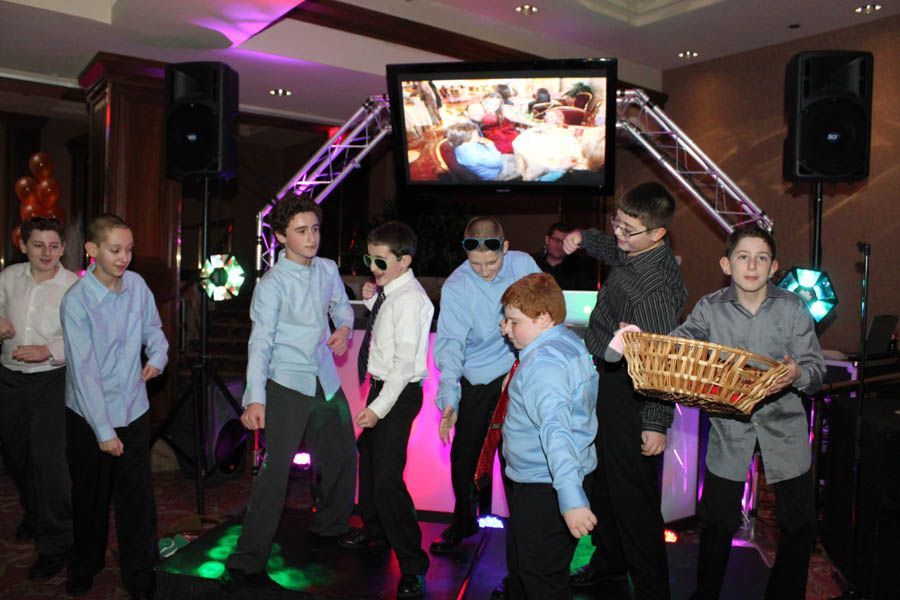 Boys dancing at an event, with music equipment, stage lights, and a screen in the background.