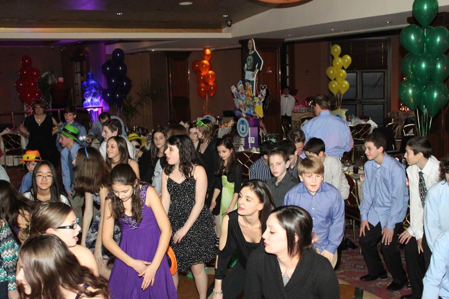 People dancing at a party with balloons. Indoors with dark walls, multi-colored lights.