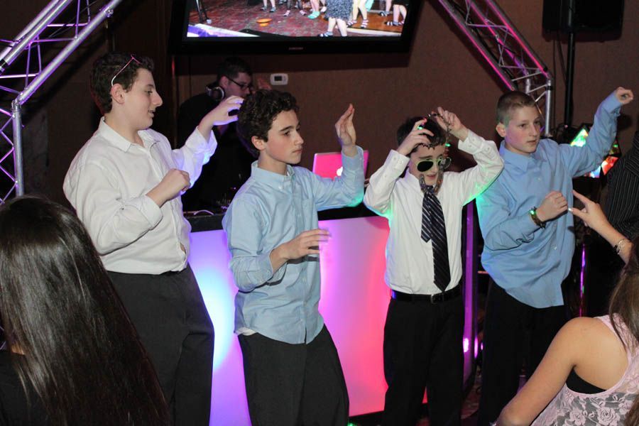 Four boys dancing at a party near a DJ booth, lit with pink and purple.