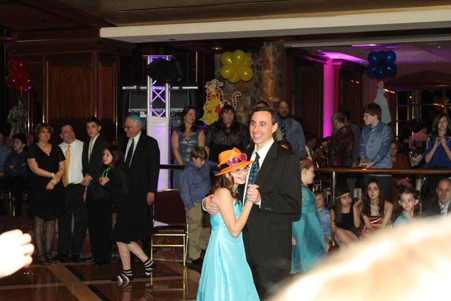Man and girl dancing at party, in ballroom with audience, festive decorations.