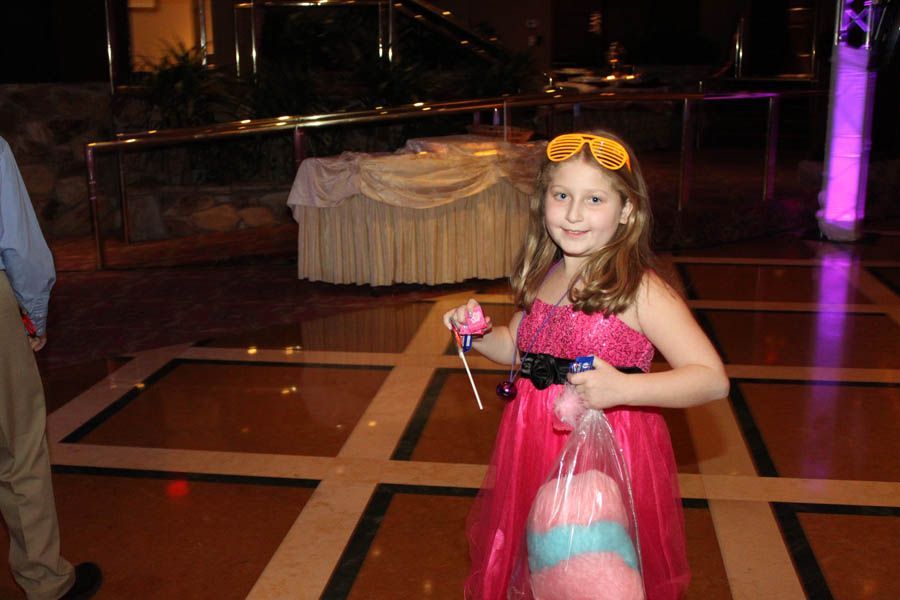 Girl in pink dress with cotton candy and sunglasses smiles on a dance floor.