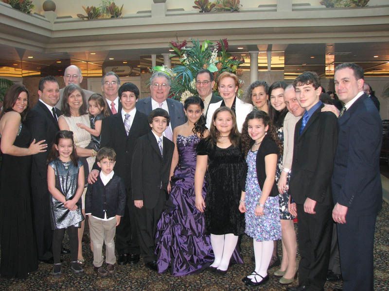 Large group posing indoors, some in formal wear. Central young woman in purple gown. Others smiling.