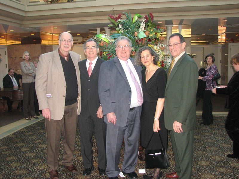 Five people pose for a photo in a hotel lobby, near a floral arrangement.