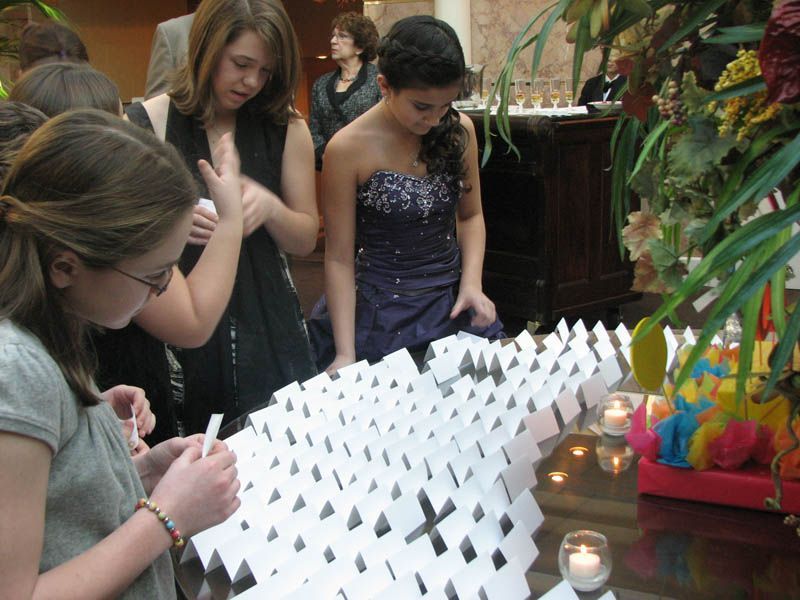 People crafting a white paper chain at a formal event, with candles and floral decorations.