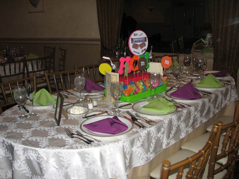 Oval table set for a party with colorful centerpieces, place settings with purple and green napkins.