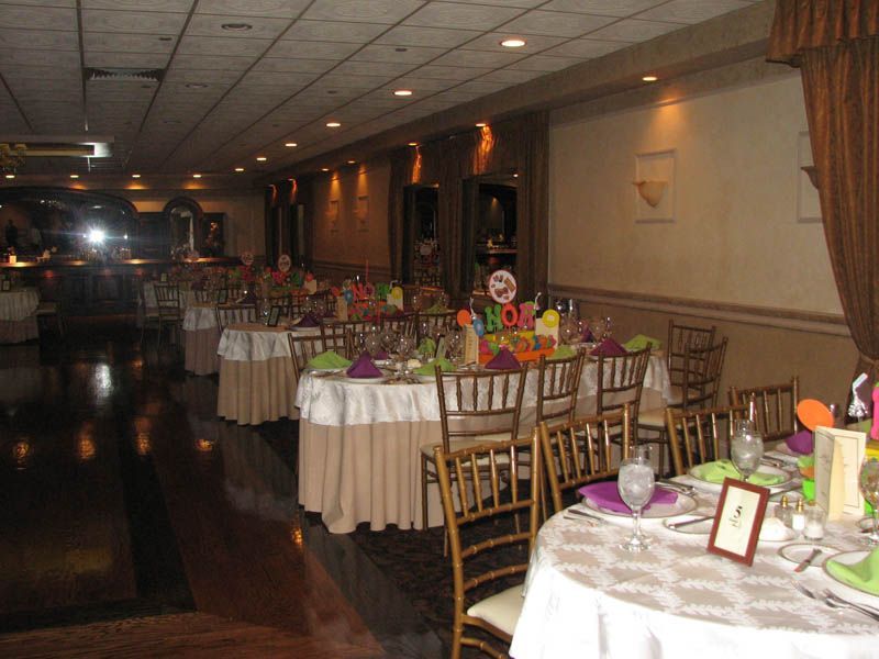 Banquet hall with tables set for a party, featuring floral centerpieces, beige tablecloths, and gold chairs.