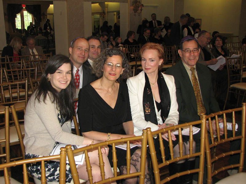 People seated in gold chairs at an event, some smiling.