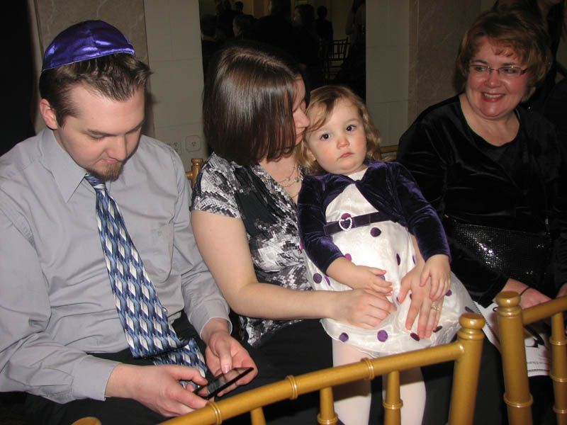 Family gathering with a man in a yarmulke, a woman holding a child, and another woman smiling.