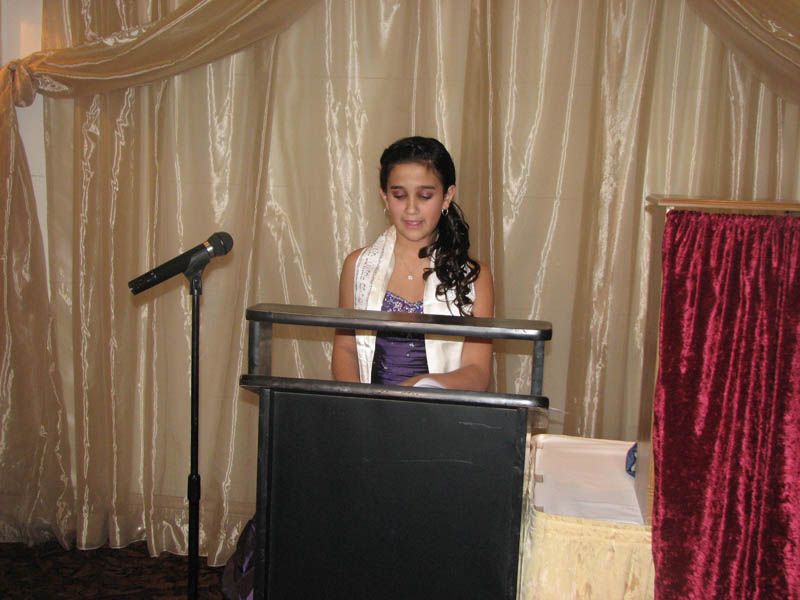Young person reading at a podium with microphone, in front of a draped curtain.