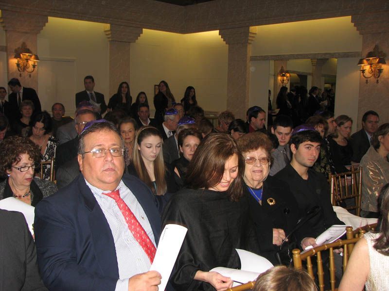 People seated, many wearing kippahs, at a formal indoor event.