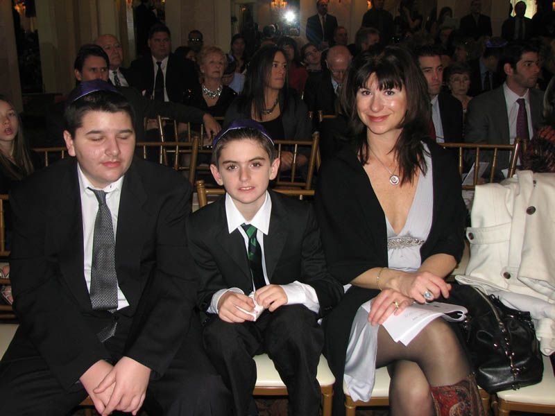 Woman and two boys in suits seated in a formal setting, possibly a Jewish ceremony.
