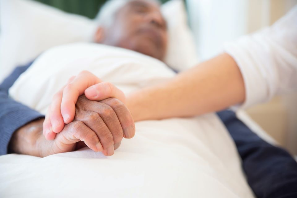 A woman is holding the hand of an elderly man in a hospital bed.