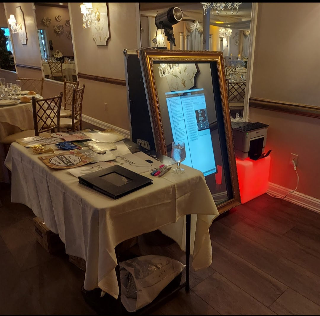 Photo booth setup at an event, with a mirror-style camera, table with props, and red-lit base.
